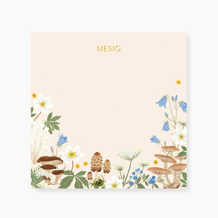 Ivory square notepad with images of flowers, mushrooms, and grass. Gold text saying, “MEMO” across the top center.