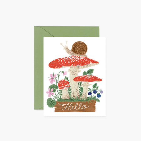 White card with images of red mushrooms, brown log, purple flowers, blueberry bush and brown snail sitting on top of mushroom. White script text saying, “Hello” on brown log. Green envelope is included.