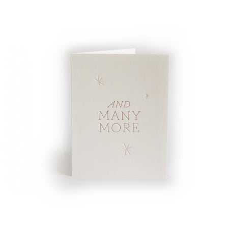 Ivory card with blush pink text saying, “And Many More”. Images of small embossed stars scattered around card. An envelope is included.
