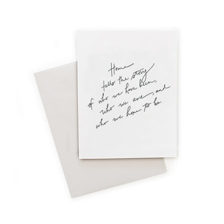 White card with black script text saying, “Home tells the story of who we have been, who we are, and who we hope to be”. A gray envelope is included.