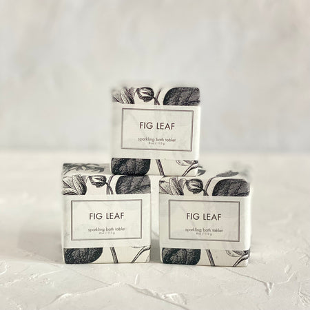 Packaged in a square white box with white label and black text saying, “Fig Leaf Sparkling Bath Cube”. Images of black fig leaves.