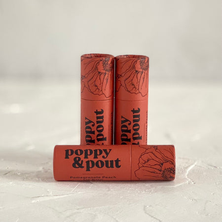 Small burnt orange tube with black text saying, “Poppy & Pout Pomegranate Peach”. Images of black poppy flowers on top of tube.