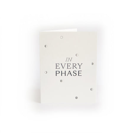 Ivory card with gray text saying, “In Every Phase”. Images of the different phases of the moon in silver. A gray envelope is included.