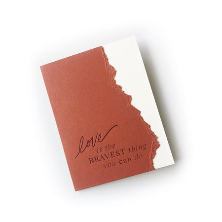 Burnt orange and white card with curved torn edge where the two colors meet with black text saying, “Love is the Bravest Thing You Can Do”. A white envelope is included.