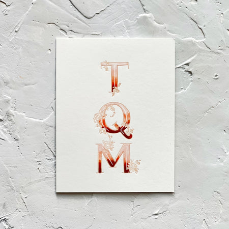 Ivory card with variegated color text in red, pink and white saying, “TQM”. Images of embossed flowers entwined around letters. An ivory envelope is included.