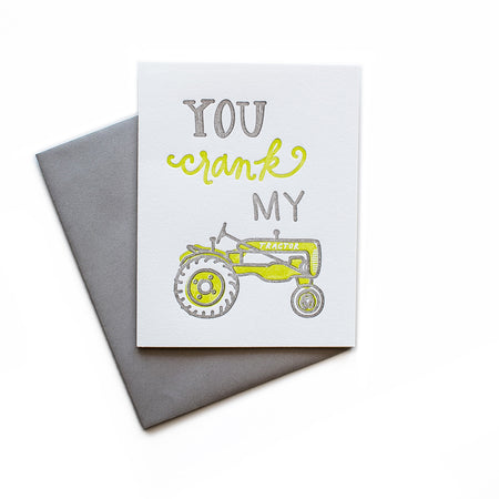 White card with gray and yellow text saying, “You Crank My Tractor”. Image of a yellow farm tractor. A gray envelope is included.