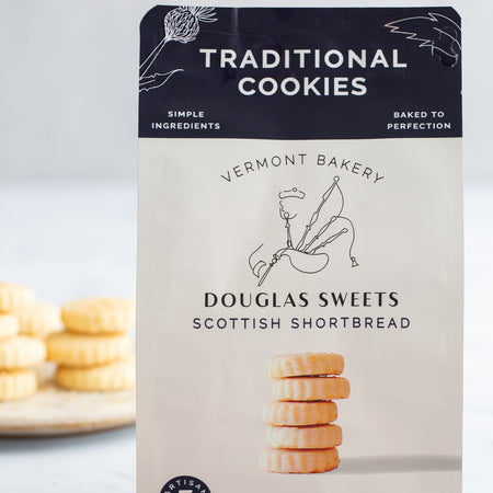 White package with black border on top with white and black text saying, “Douglas Sweets Vermont Bakery Scottish Shortbreads Traditional Cookies”. Image of a stack of shortbread cookies and outline of a man playing bagpipes.