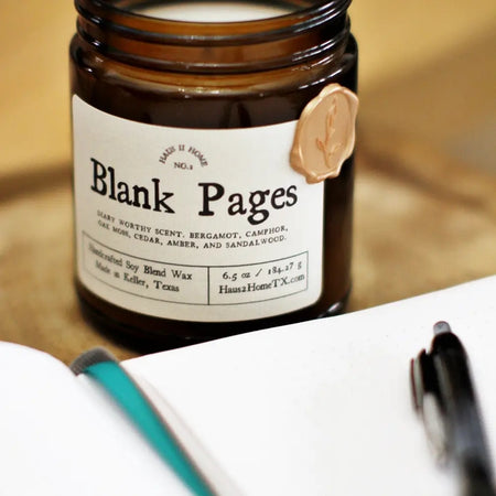 Amber color jar candle with gold lid. White label with black text saying, “Blank Pages”.