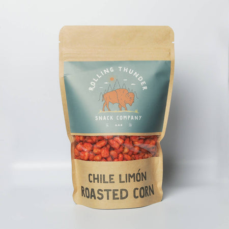 Tan bag with silver label with white text and black text saying, “Rolling Thunder Snack Company Chile Limon Roasted Corn”. Image of a brown buffalo in center of label. Clear strip across middle to see product inside. Brown roasted corn.