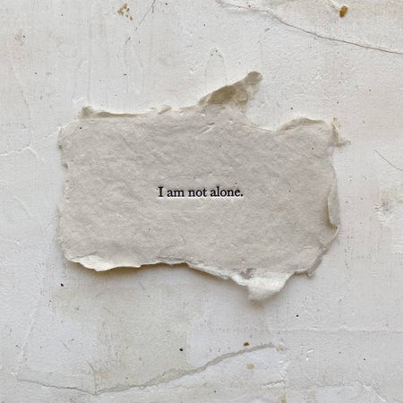 Gray rectangle with torn edges and black text saying, “I am Not Alone”.
