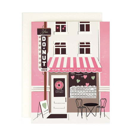 Ivory card with image of a city building block with a donut shop. Windows up above and a pink and white awning saying, “You Donut Know How Much I Love You”. An ivory envelope is included.