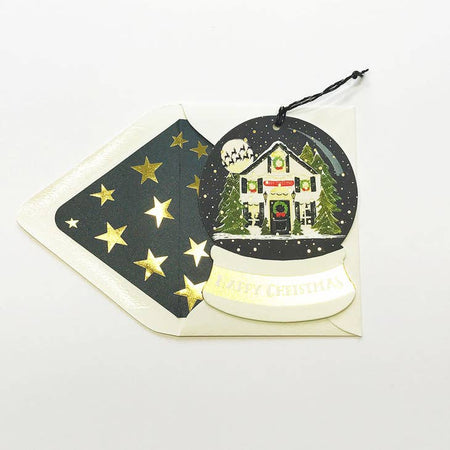 Card in the shape and image of a snow globe with a decorated Christmas house with green pine trees around it and a full moon in the sky with shadows of reindeer across. An ivory envelope is included.