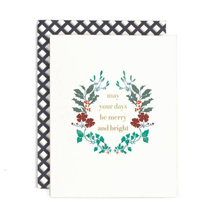 White card with image of a holly wreath in center. Gold foil text saying, 