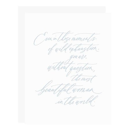 White card with blue text saying, “Even in these moments of wild exhaustion, you are, without question, the most beautiful woman in the world”. A gray envelope is included.