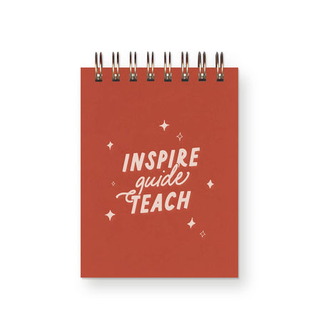 Orange cover with white text saying, “Inspire Guide Teach”. Metal spiral coil binding across top.