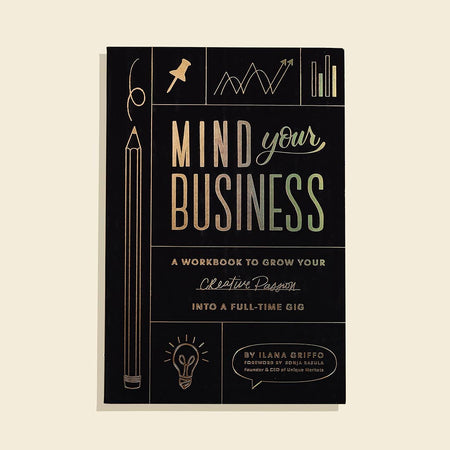 Black cover with gold foil text saying, “Mind Your Business A Workbook to Grow Your Creative Passion Into a Full-Time Gig”. Images of a pencil, lightbulb, pushpin, and bar graph in gold foil.