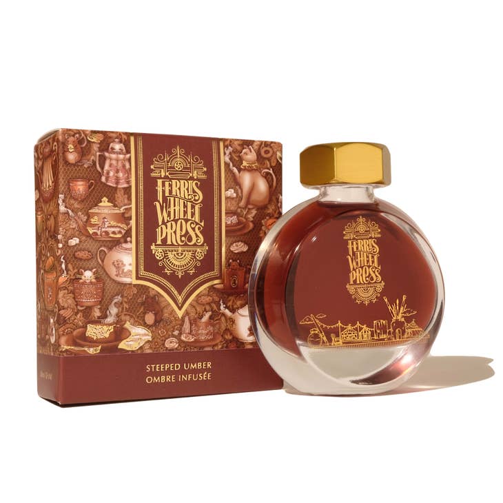Round glass bottle with gold cover and gold text saying, "Ferris Wheel Press" with images of a carnival on front of bottle. Ink is brown. Packaged in square brown box with images of teapots.