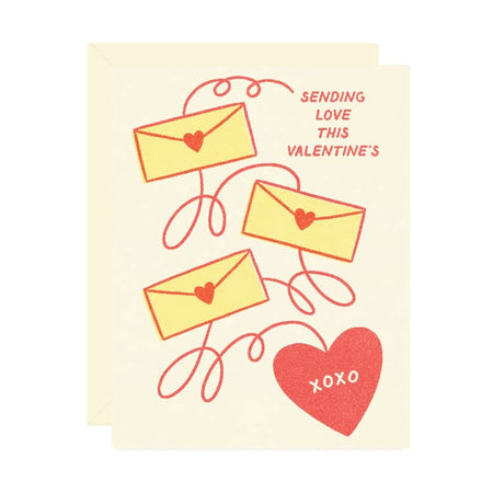 White card with images of yellow envelopes attached to a red heart with red squiggly lines. Red text saying, “Sending Love this Valentine’s”. A white envelope is included.