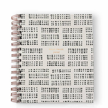 Notebook with ivory and black dots cover with gold foil text saying, “Daily Pause Journal”. Gold coil binding on left side.