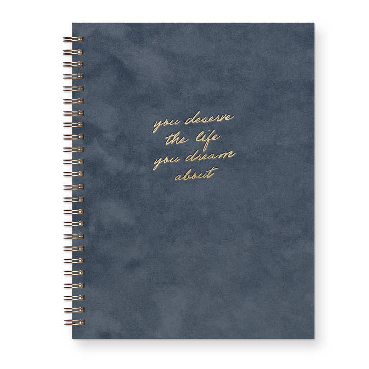 Notebook with midnight blue suede cover with gold foil text saying, "You Deserve the Life You Dream About". Metal coil binding on left side.