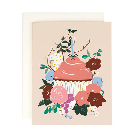 Ivory card with image of a birthday cupcake with pink frosting and blue birthday candle. Cupcake is surrounded by various colored flowers. An ivory envelope is included.