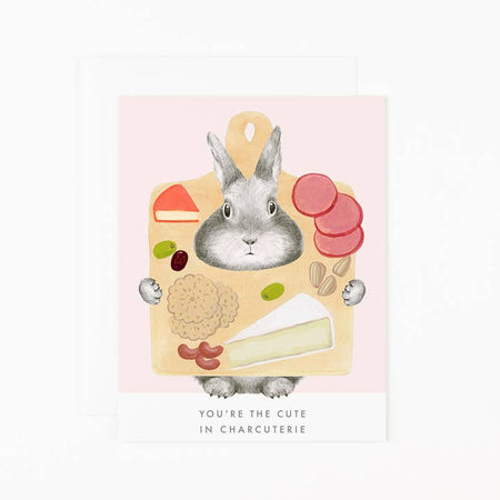 White card with image of a gray bunny holding a charcuterie board. Gray text saying, “You’re the Cute in Charcuterie”. A white envelope is included.
