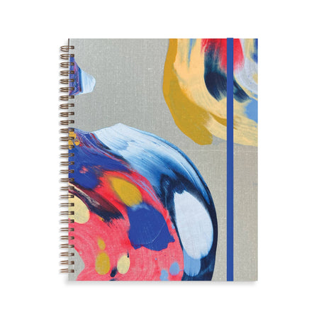 Notebook with gray cover with black, blue, white, pink, yellow and green brushstroke abstract pattern. Metal coil binding on left side. Blue elastic over right side.