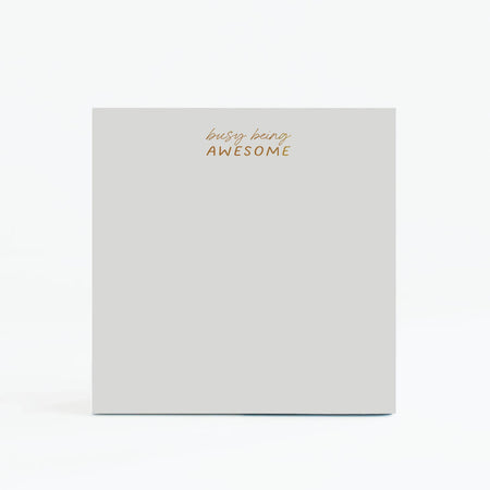 Gray square notepad with gold foil text saying, “Busy Being Awesome” in top center.