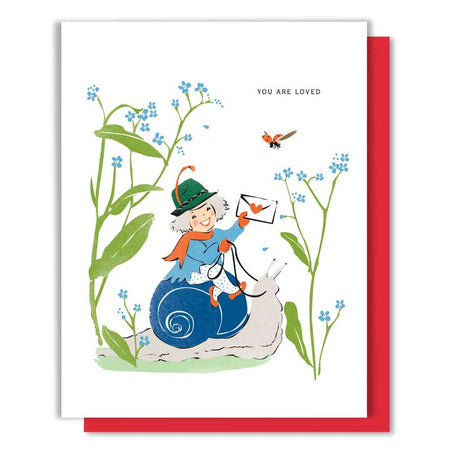 White card with images of a woman riding on a snail holding a red heart envelope in her hand with blue flowers in the background. Black text saying, “You Are Loved”.  A red envelope is included.