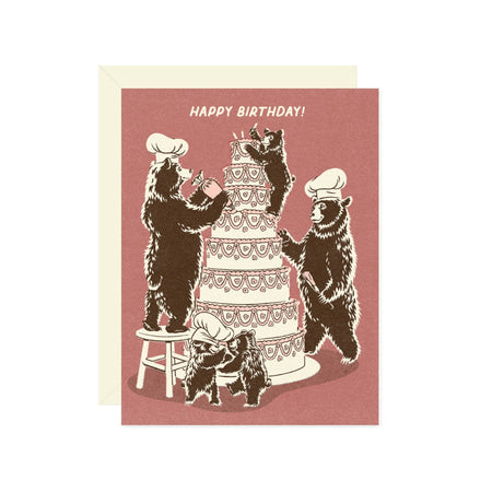 Purple card with white text saying, “Happy Birthday”. Images of several brown bears dressed as bakers decorating an 8 tiered birthday cake. A cream envelope is included.