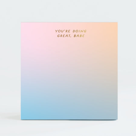 Rainbow ombre square notepad with gold foil text saying, “You’re Doing Great, Babe” in top center.
