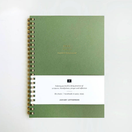 Moss green cover with gold foil text saying, “Pray A Guided Daily Journal”. Gold coil binding on left side.