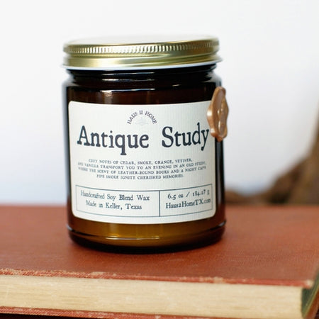 Amber color jar candle with gold lid. White label with black text saying, “Antique Study”.