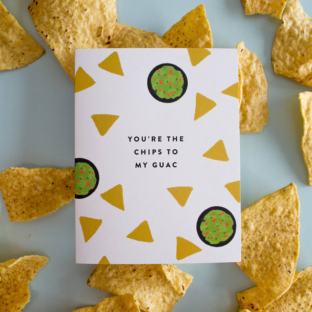 White card with black text saying, “You’re the Chips to My Guac”. Images of bowls of guacamole and yellow tortilla chips scattered around card. A white envelope is included.