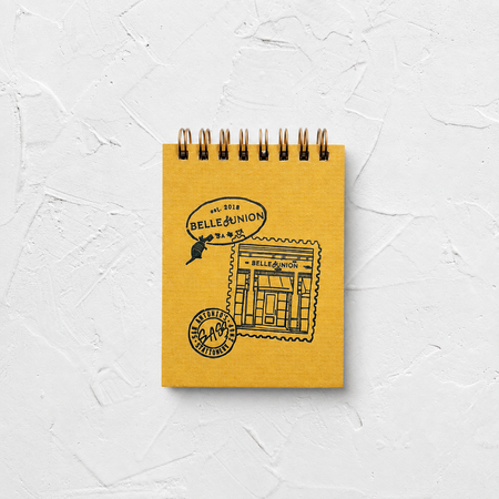 Yellow spiral bound jotter with gray Belle & Union branded text, on white textured background.