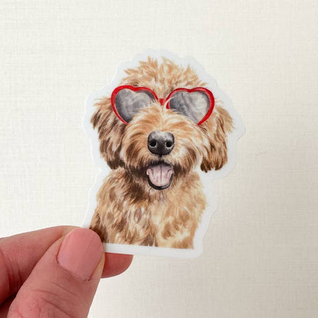 Sticker in the image of a golden doodle dog wearing red heart shaped sunglasses.