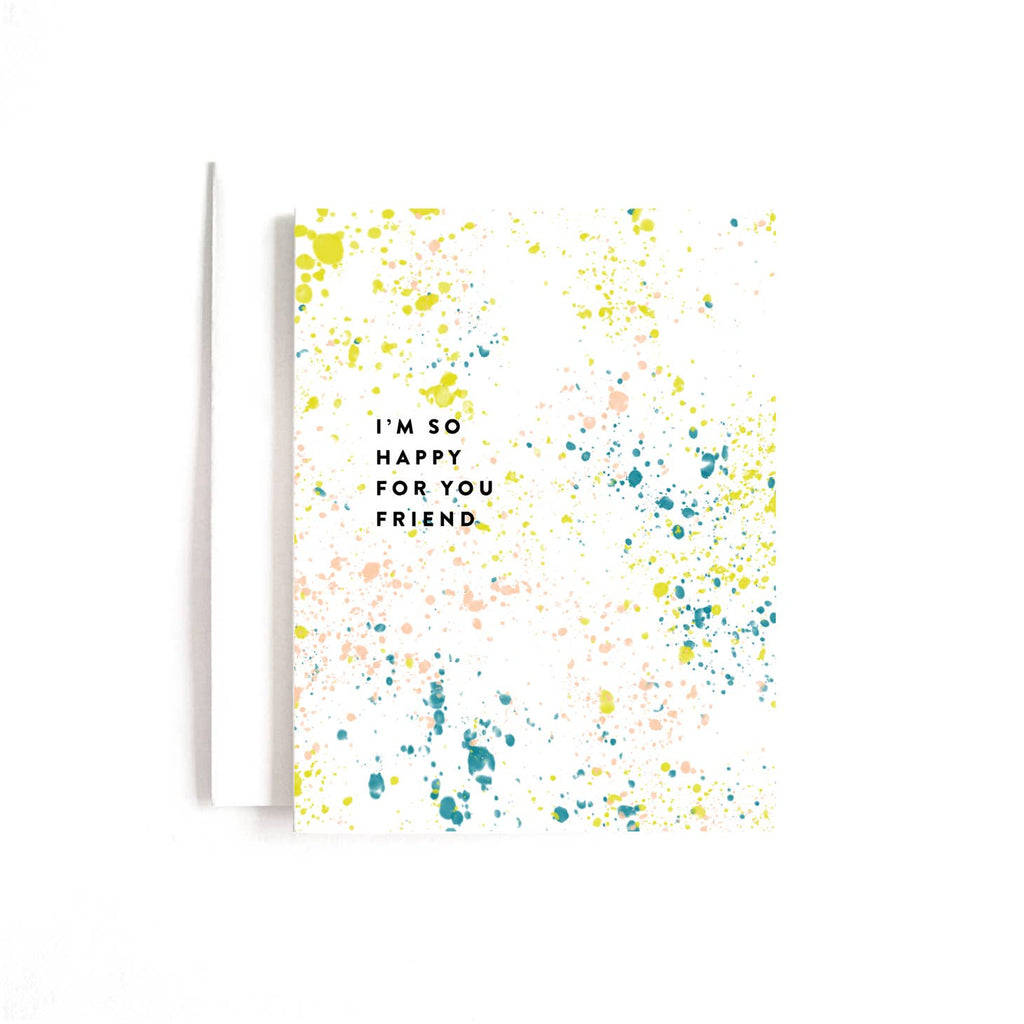White card with colorful paint splatters across card. Black text saying, “I’m So Happy For You Friend”. A white envelope is included.