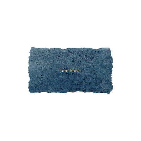 Blue rectangle with torn edges and gold foil text saying, “I am Brave”.