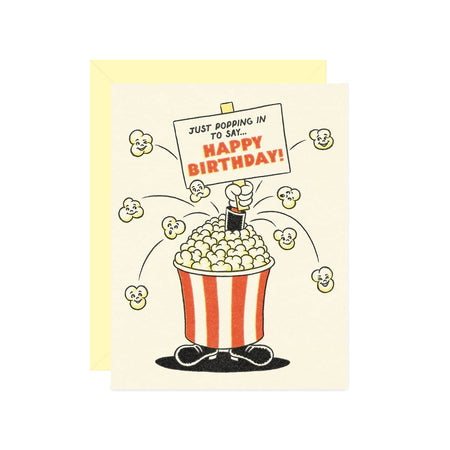 Ivory card with image of a bucket of popcorn wearing black shoes and holding a sign saying, “Just Popping In to Say… Happy Birthday”. A cream envelope is included.