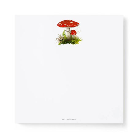White square notepad with image of a red mushrooms and green moss in top center of pad.