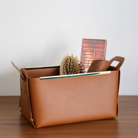 Brown leather soft sided box with handles and gold metal strips along the two sides.