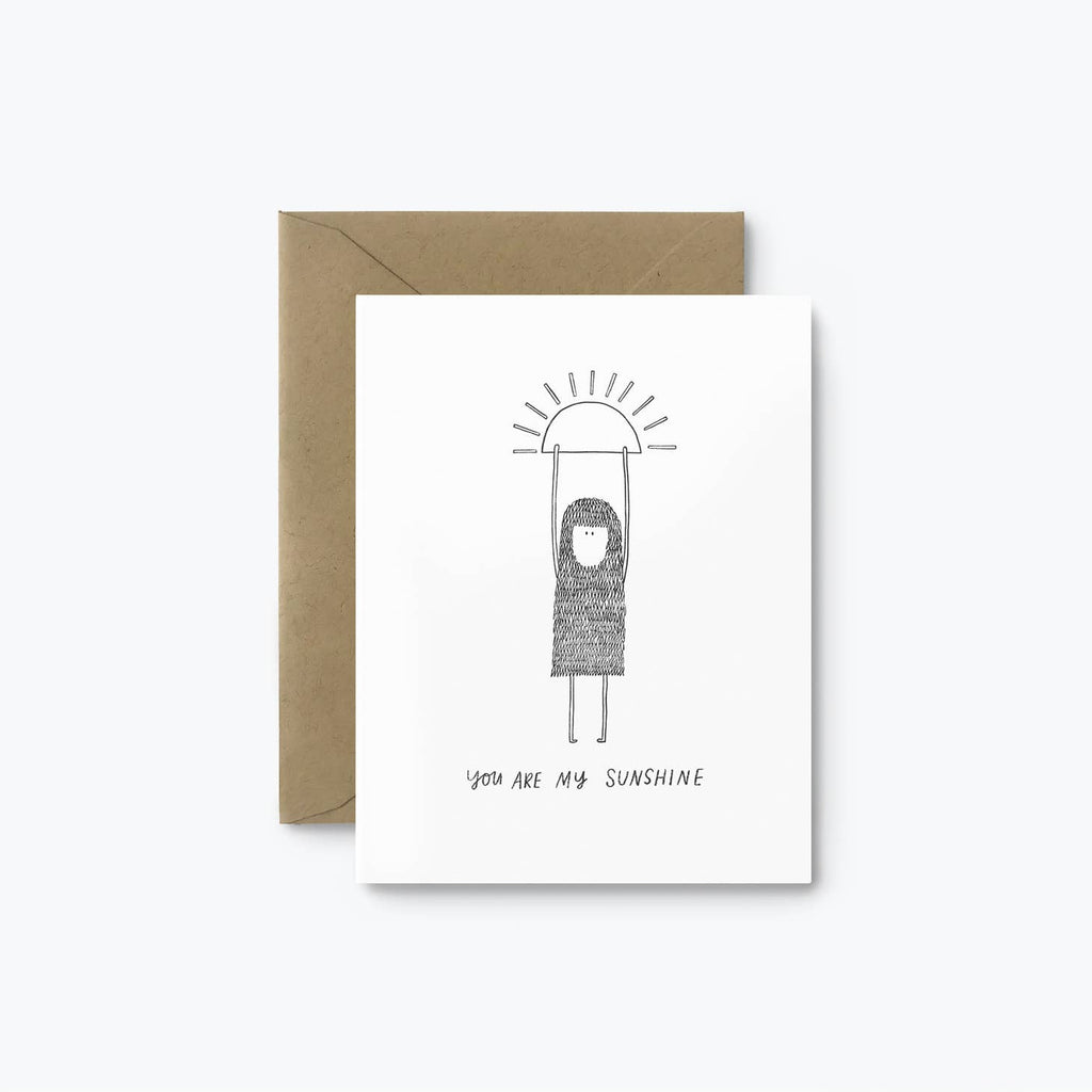 White card with image of a hand illustrated woolie creature hanging from the sun with text that reads “You Are My Sunshine”. A brown kraft envelope is included.