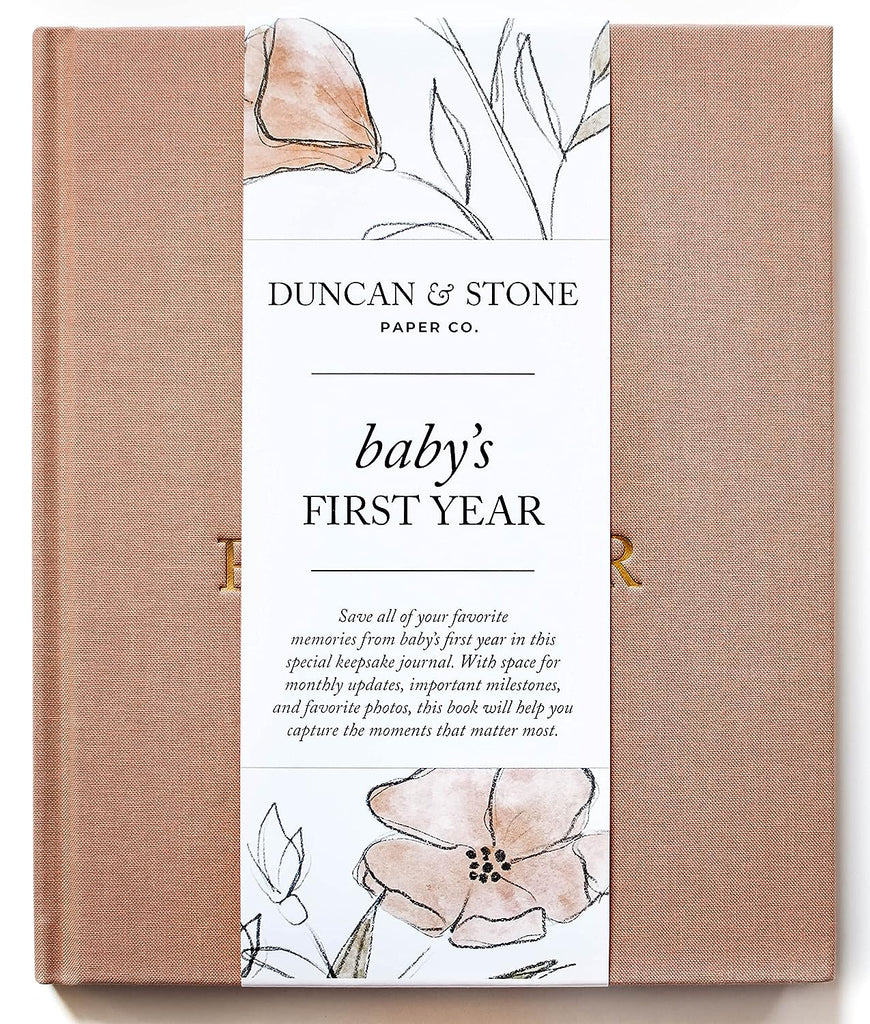   Dusty rose color journal with gold foil text saying, “Baby’s First Year” in center.