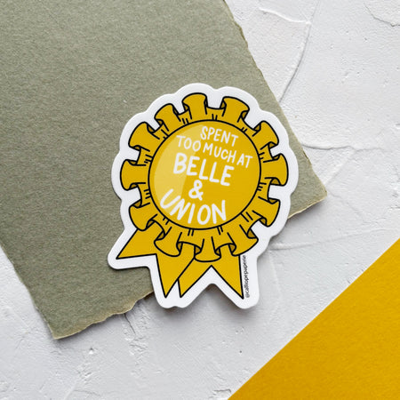 Sticker of yellow ribbon with white text, on green textured paper. 