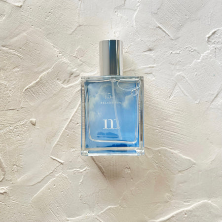 Square clear glass bottle with silver lid. White text saying, “No 53 Relaxation”. Blue background inside bottle.