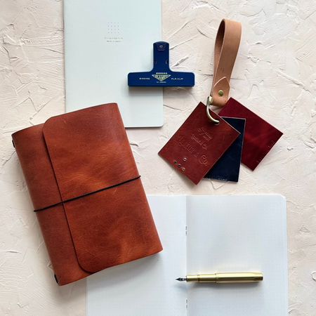 Leather-bound notebook with pen, stamp, and leather pieces on a textured surface
