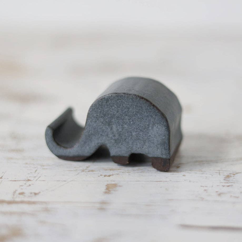 Gray phone stand in the shape of an elephant with the trunk curved to hold phone.