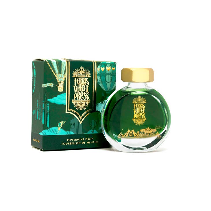Round glass bottle with gold cover and gold text saying, "Ferris Wheel Press" with images of a carnival on front of bottle. Ink is green. Packaged in square green box with images of hot air balloons.