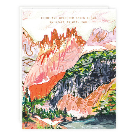 Ivory card with gold foil text saying, “There Are Brighter Skies Ahead. My Heart is With You.” Image of a mountain landscape. A white envelope is included.
