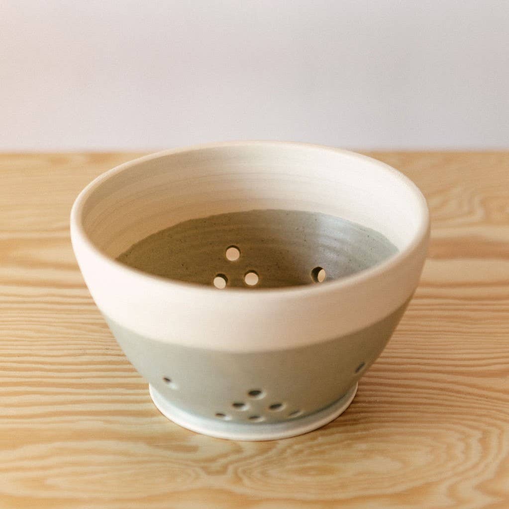 White and gray ceramic bowl with decorative holes drilled into sides to function as a strainer for holding and washing berries.